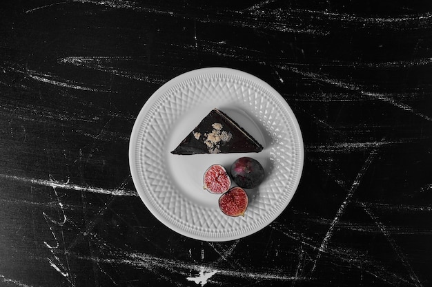 A slice of chocolate cake in a white plate with figs aside.