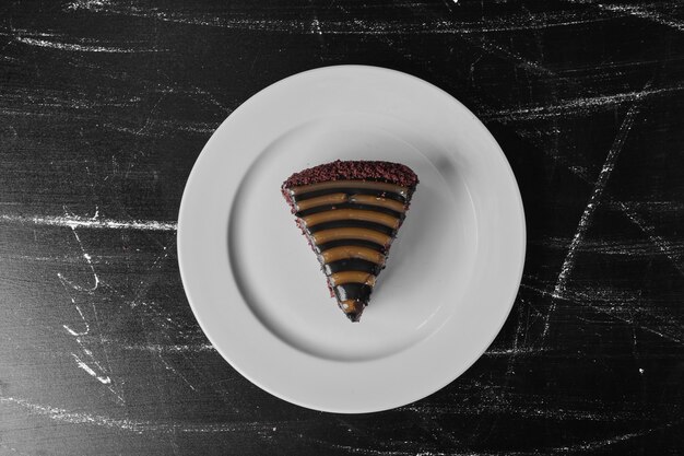 A slice of chocolate cake in a white plate with ganache on the top.