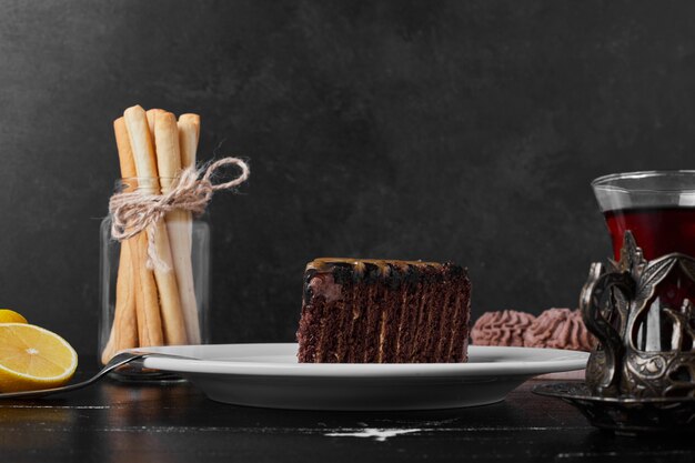 A slice of chocolate cake in a white plate with a glass of tea.