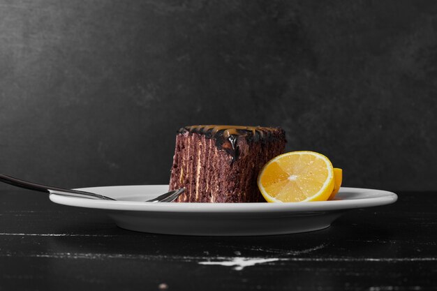 A slice of chocolate cake in a white plate with lemon slices.