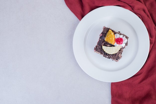 Slice of chocolate cake on white plate with red tablecloth.