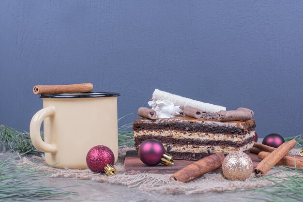 A slice of chocolate cake with a cup of drink and christmas decorations around