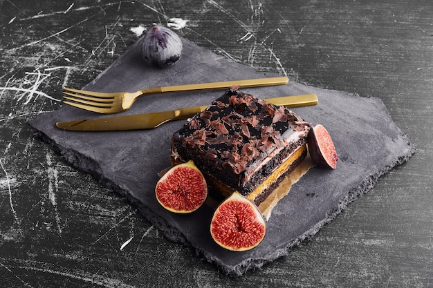 A slice of chocolate cake with figs on a stone platter. 