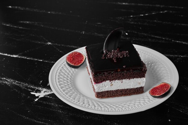 A slice of chocolate cake with fruits aside in a white plate.