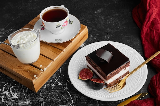 A slice of chocolate cake with fruits and a cup of tea and curd. 