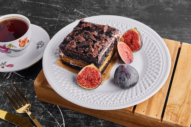 Кусочек шоколадного торта с фруктами и чашка чая в белой тарелке.