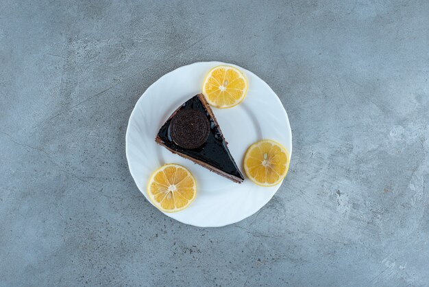 Кусочек шоколадного торта с ломтиками лимона на белой тарелке. Фото высокого качества