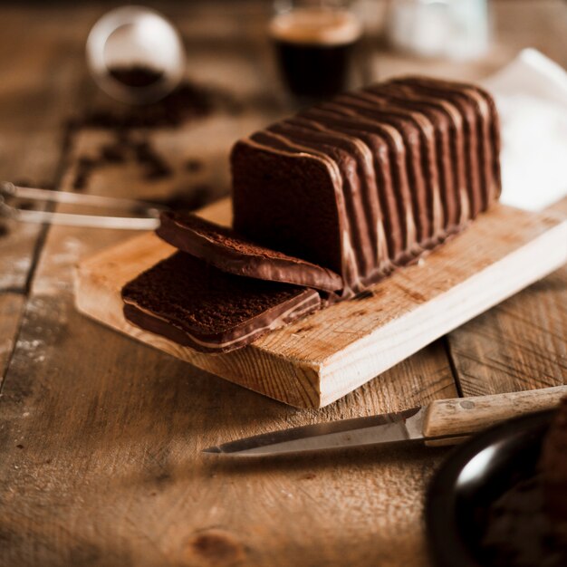 Slice of chocolate cake on wooden board with sharp knife