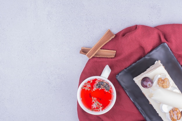 A slice of coconut cake with grape and walnut served with a cup of herbal tea