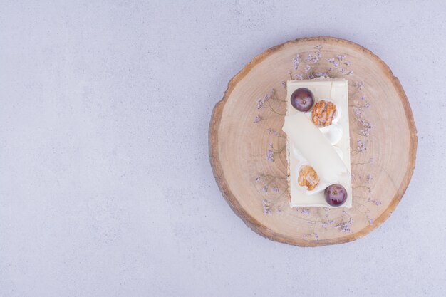 A slice of coconut cake with grape and walnut on a wooden board