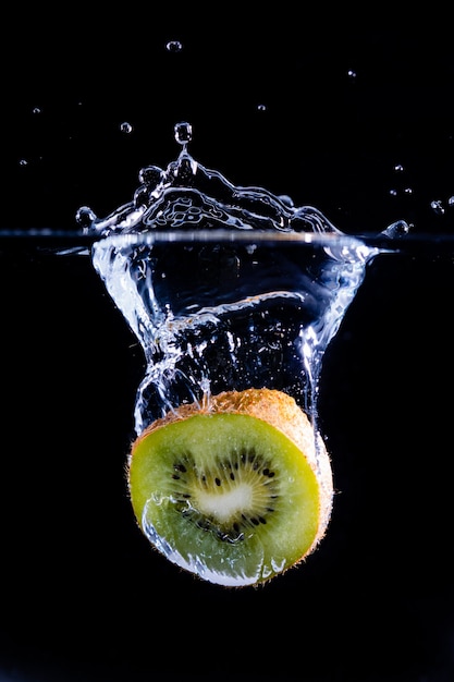 Slice of fresh kiwi splashing in the water with a black