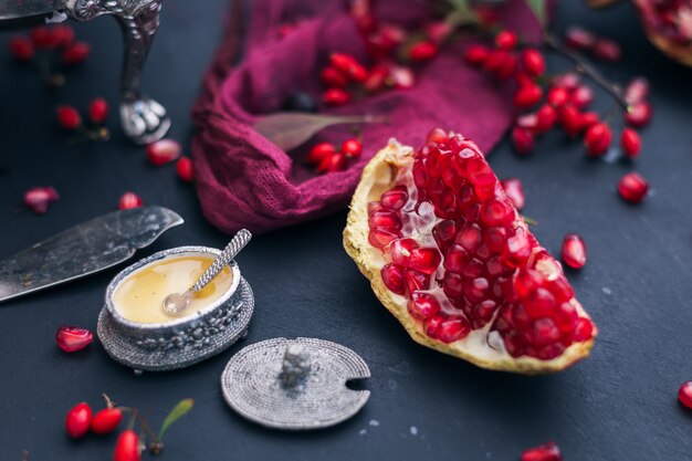 Slice of fresh pomegranate surrounded by its seeds placed on a blue smooth surface