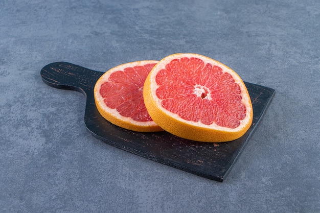 Нарезать грейпфрут на разделочной доске на мраморном фоне.