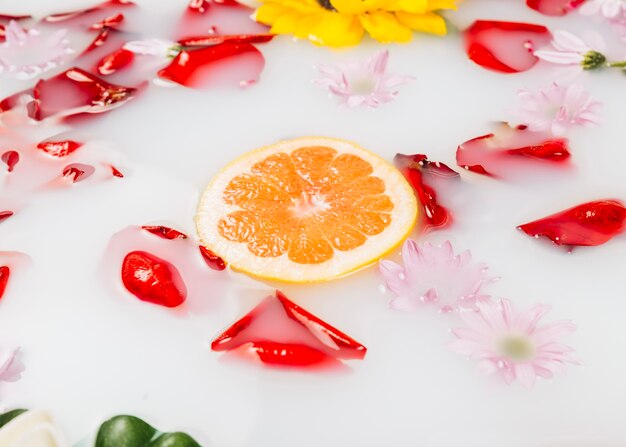 Slice of grapefruit surrounded with flowers and petals on milk