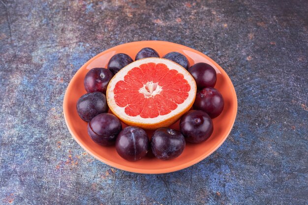 Slice of grapefruit with delicious plums placed in an orange plate .