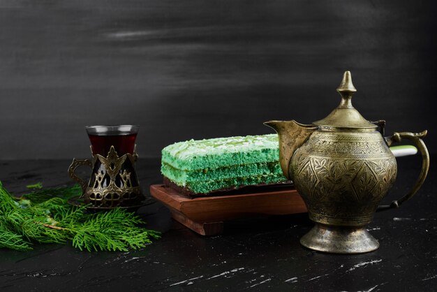 A slice of green cake with a glass of tea. 