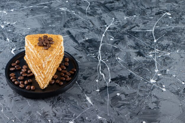 Slice of layered honey cake with coffee beans placed on a marble table.