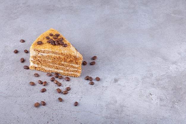 Slice of layered honey cake with coffee beans placed on a stone background . 