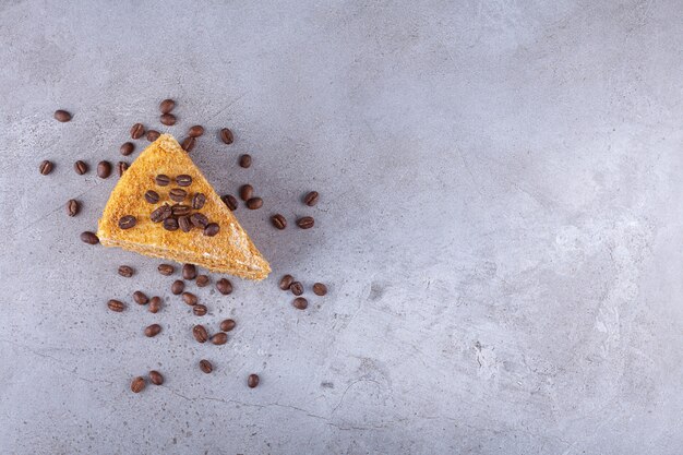 Slice of layered honey cake with coffee beans placed on a stone .