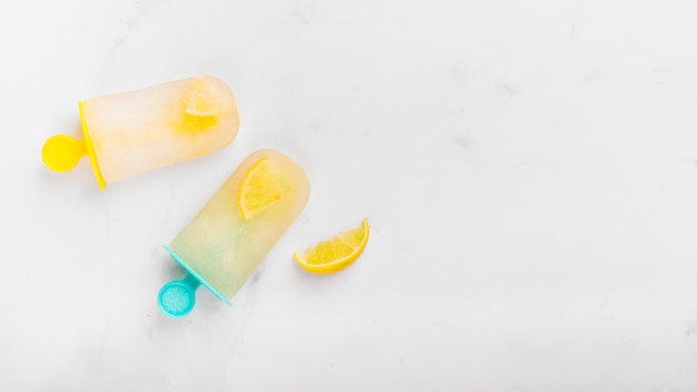 Slice of lemon and cold ice popsicle with citrus on colorful sticks