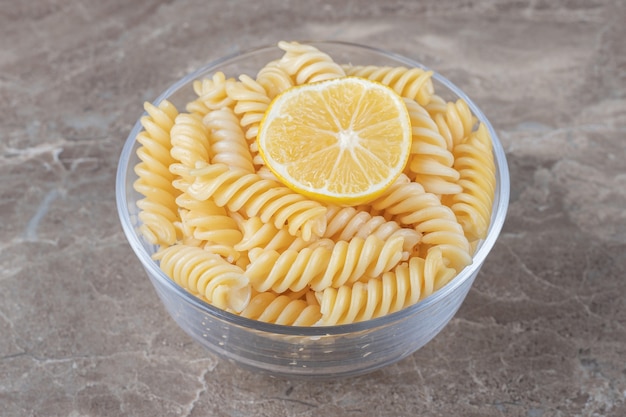 A slice of lemon in the fusilli pasta on the bowl , on the marble surface.