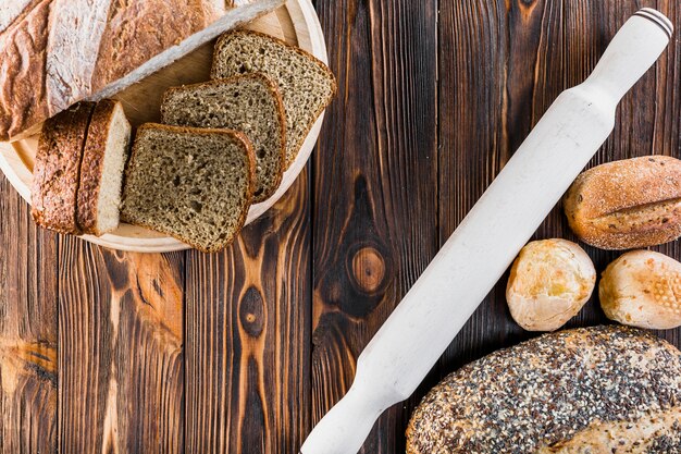 Ломтик и буханки хлеба с скалкой на деревянном столе