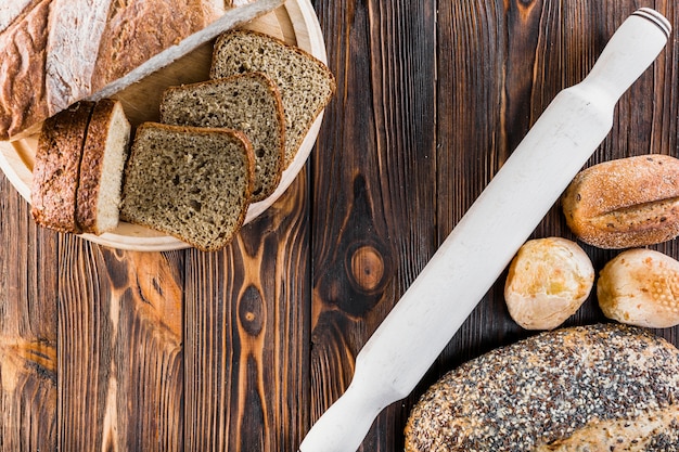 Slice and loaves of bread with rolling pin on wooden desk