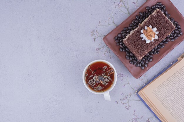 A slice of medovic cake with chopped chocolate in a platter with a cup of herbal tea