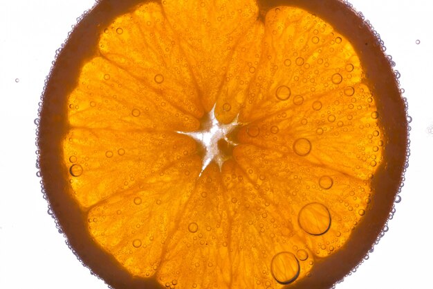 Ломтик оранжевого плавает в воде на белом фоне