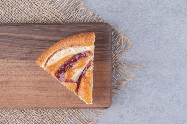 A slice of pie on a wooden board on marble table.