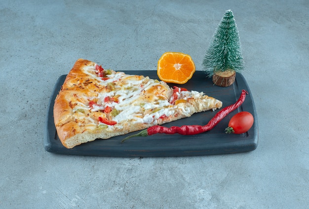 Free photo a slice of pizza on a board with a tree figurine on marble surface