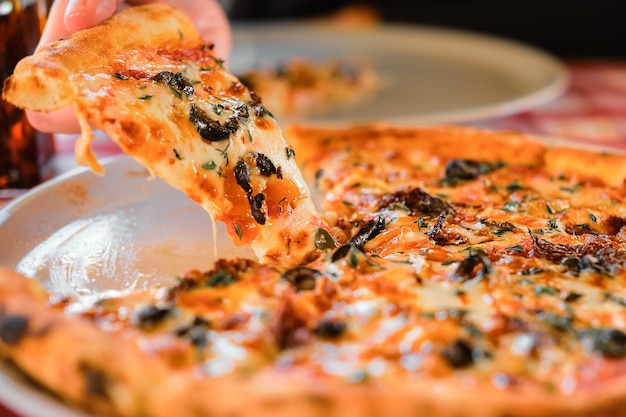手のクローズ アップのピザのスライス セレクティブ フォーカス トラットリアでの昼食の時間 ピッツェリアでモッツァレラチーズをスライスしたサンドライ トマトのおいしいピザ ランチ