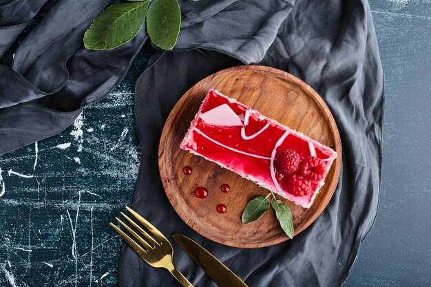 A slice of red cheesecake on a wooden platter, top view. 