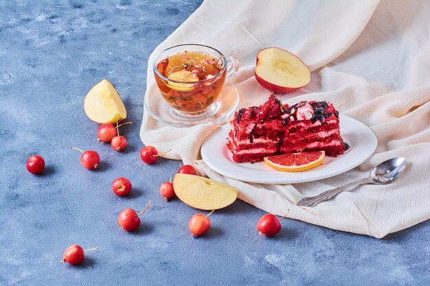 A slice of red velvet cake in a white plate with tea.