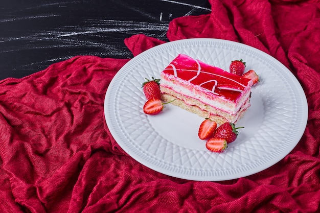 A slice of strawberry cake on a white plate on dark background. 