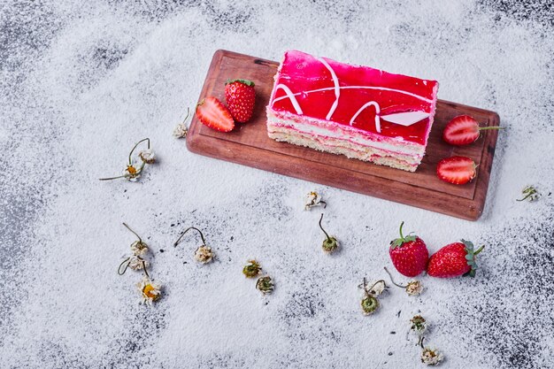 A slice of strawberry cake with dried daisies on wooden board. 