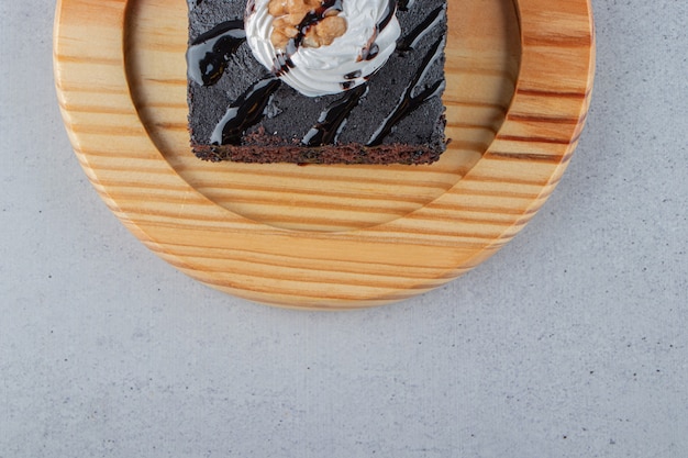 Slice of tasty chocolate brownie with cream on wooden plate. High quality photo