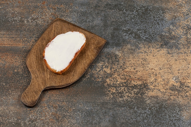 Slice of toast with sour cream on wooden board.