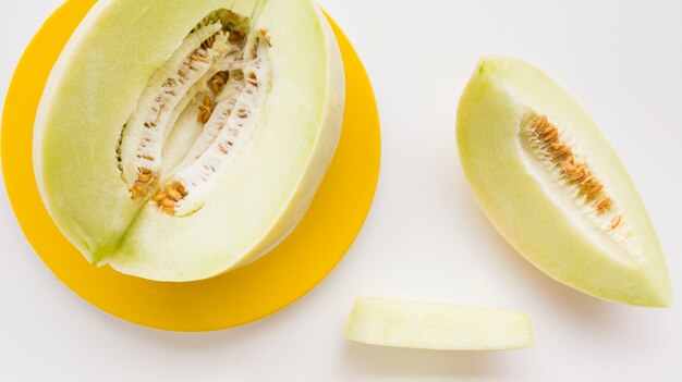 Slice and whole muskmelon on yellow plate over white backdrop
