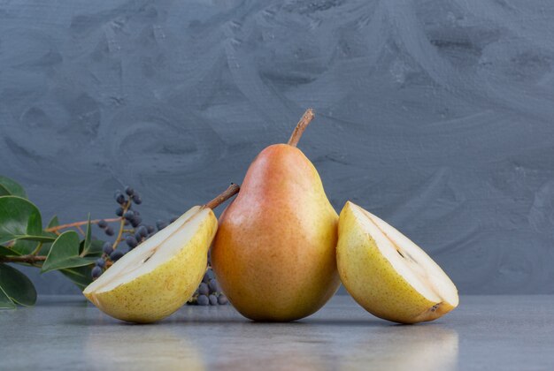 Slice and whole pears next to a decorative branch on marble background. 