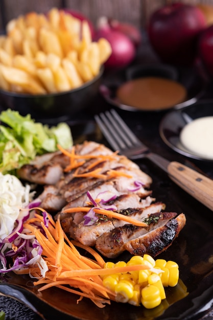 Sliced ââpork steak with bread, carrots, cauliflower, lettuce and corn on a black plate.