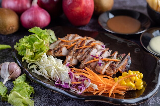 Sliced ââpork steak with bread, carrots, cauliflower, lettuce and corn on a black plate.