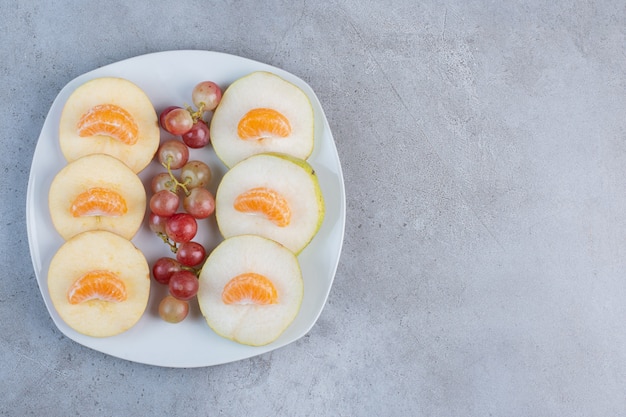 Free photo sliced apples, pears, tangerines and grapes on a platter on marble background.