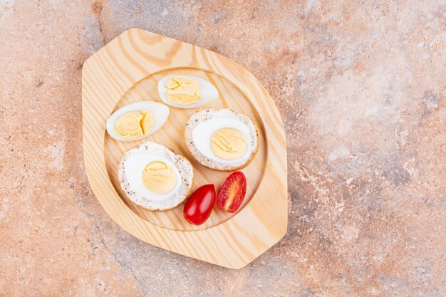 Sliced boiled egg, tomatoes and bread on a wooden plate, on the marble.