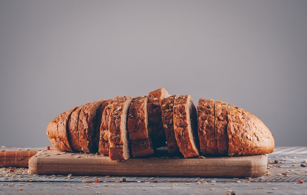 Отрезанный хлеб на разделочной доске на деревянном столе и сером поверхностном взгляде со стороны.