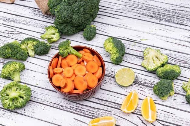 sliced carrot in ceramic bowl with broccoli on white wooden surface