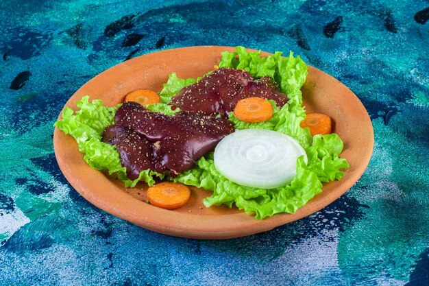 Sliced carrot, onion lettuce leaves and chicken liver on a clay bowl