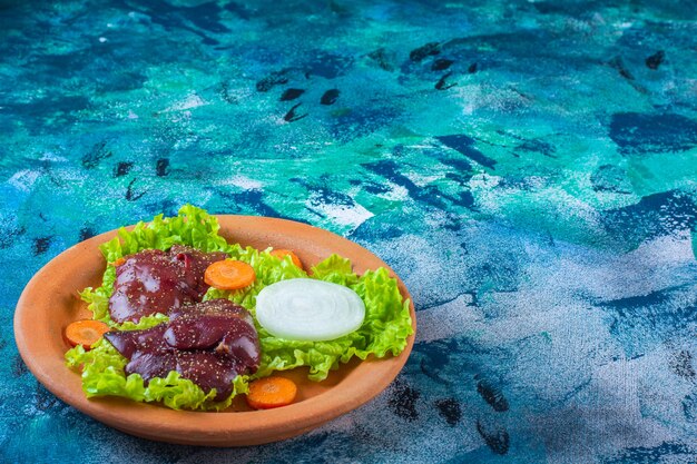 Sliced carrot, onion lettuce leaves and chicken liver on a clay bowl