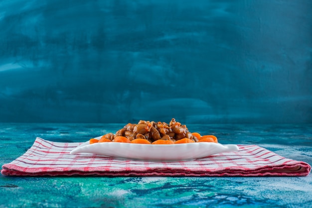 Sliced carrots and beans on a plate on the tea towel , on the blue background. 