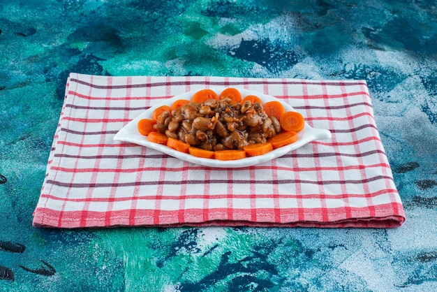 Sliced carrots and beans on a plate on the tea towel , on the blue table